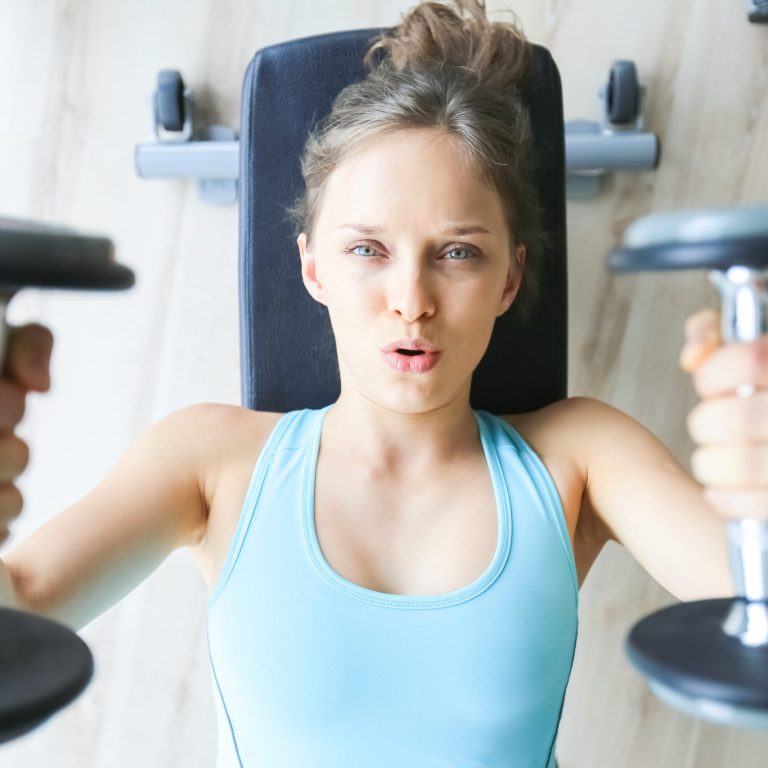 Closeup of serious young pretty woman wearing sportswear, lying and training with two dumbbells in gym. Top view.